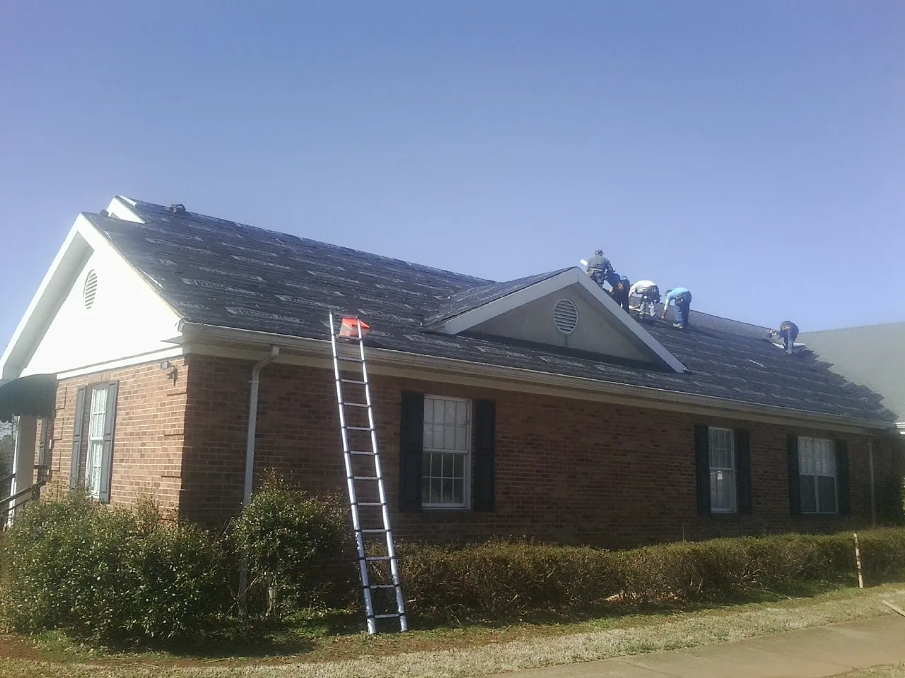 Crew tearing shingles off a brick ranch roof with a ladder set — Metal Roof Repair work by our crew in South Elgin