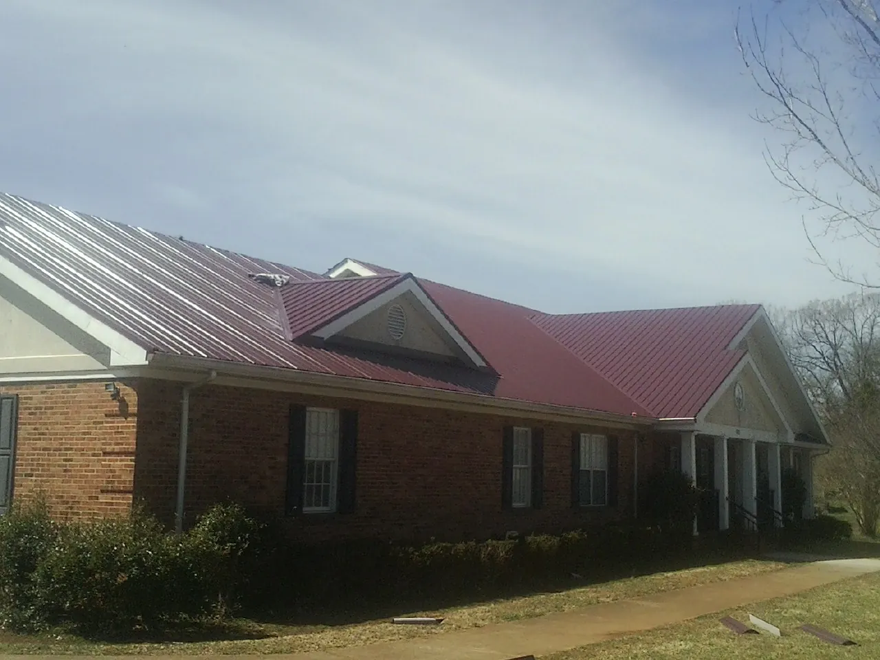 Red metal roof with gabled entries on a long brick building, from a Hail Damage Roof Repair job in South Elgin