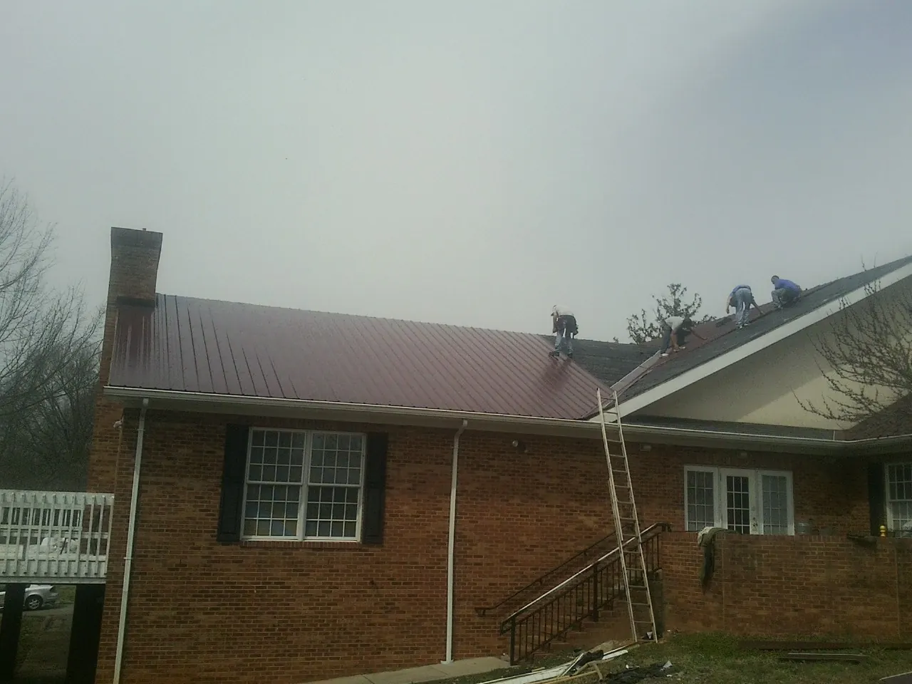 Crew setting red metal roofing panels on a brick home in South Elgin