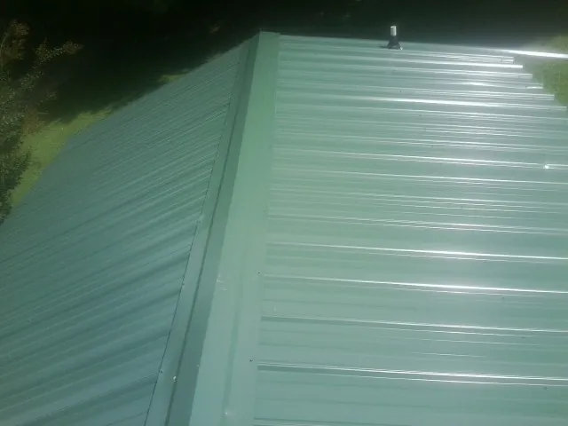 New green metal panels meeting at the ridge of a roof — Flat Roof Repair work by our crew in South Elgin