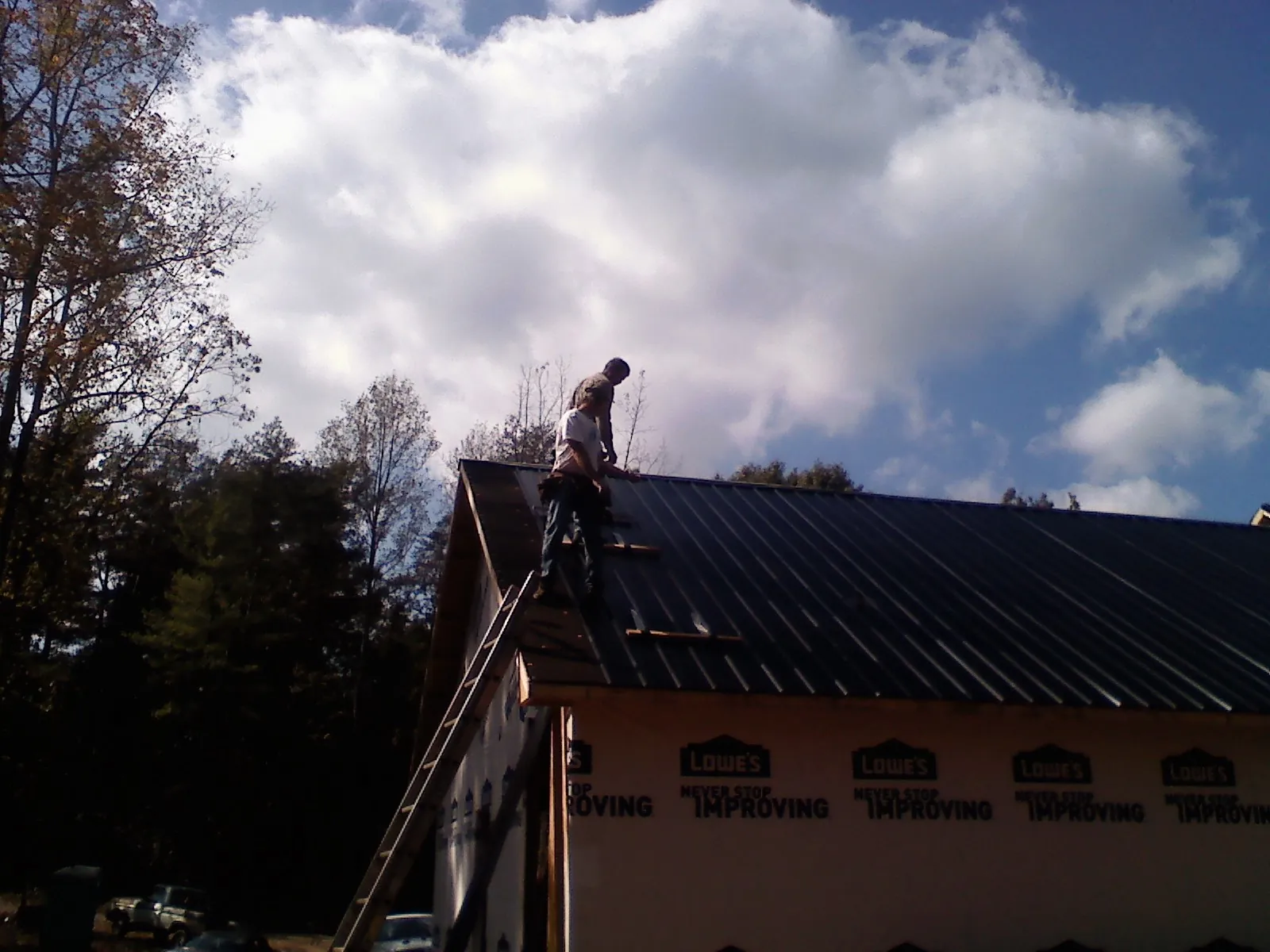 Roofer fastening dark metal panels high against a cloudy sky, from a Roof Inspection job in South Elgin