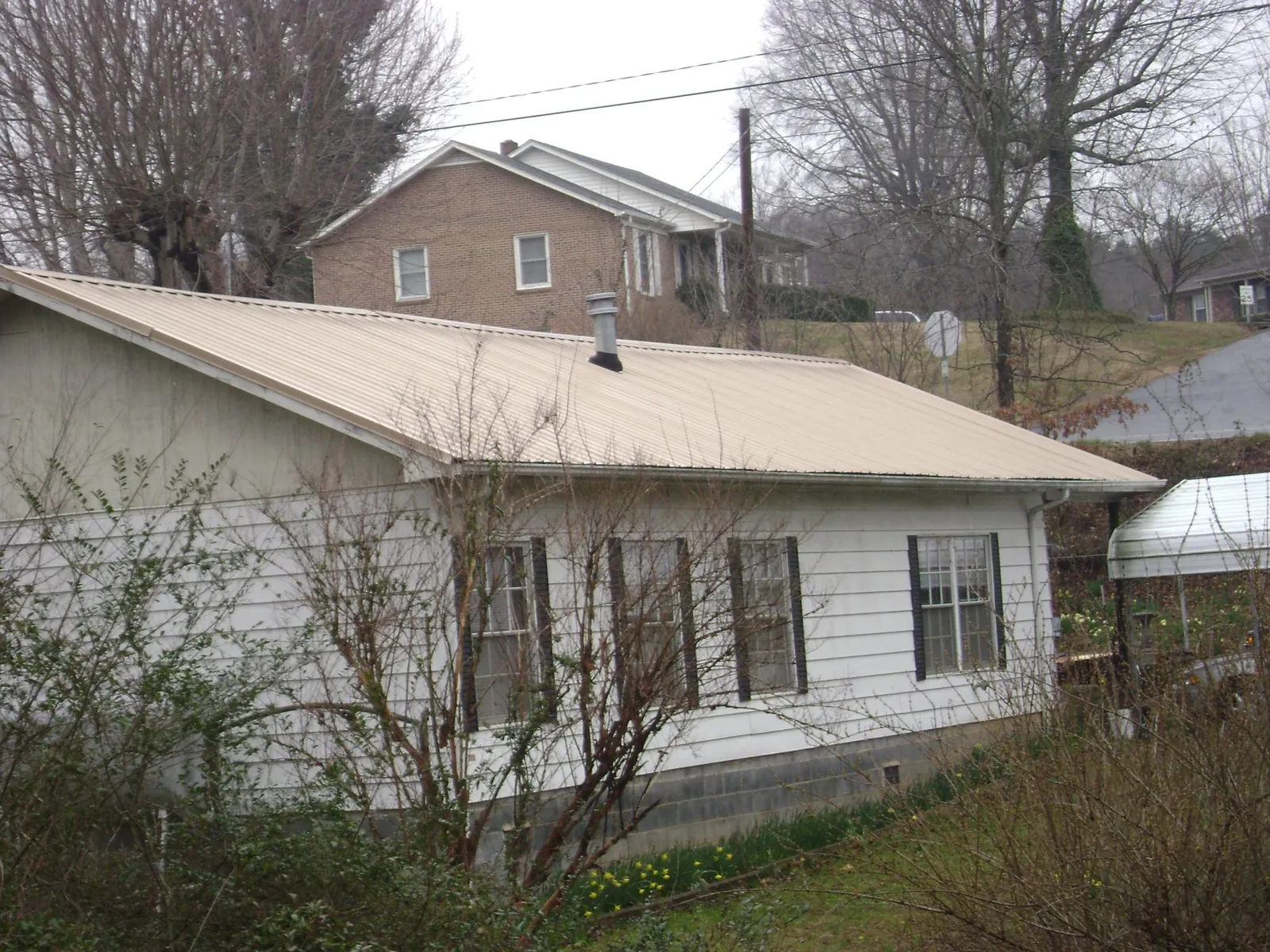 Tan metal roof on a white sided house set into a hillside — Commercial Roofing by Roofing Brothers in South Elgin